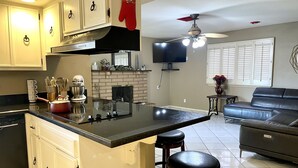 A modern kitchen with a large island, white cabinets, and a red oven mitt. There is a fireplace, a ceiling fan, and a living area with a leather couch.