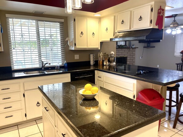 A modern kitchen with white cabinets, a black granite countertop, and a red stool.