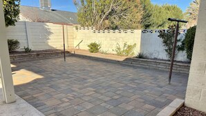 A paved patio area with a brick floor, surrounded by a low wall and a white fence.