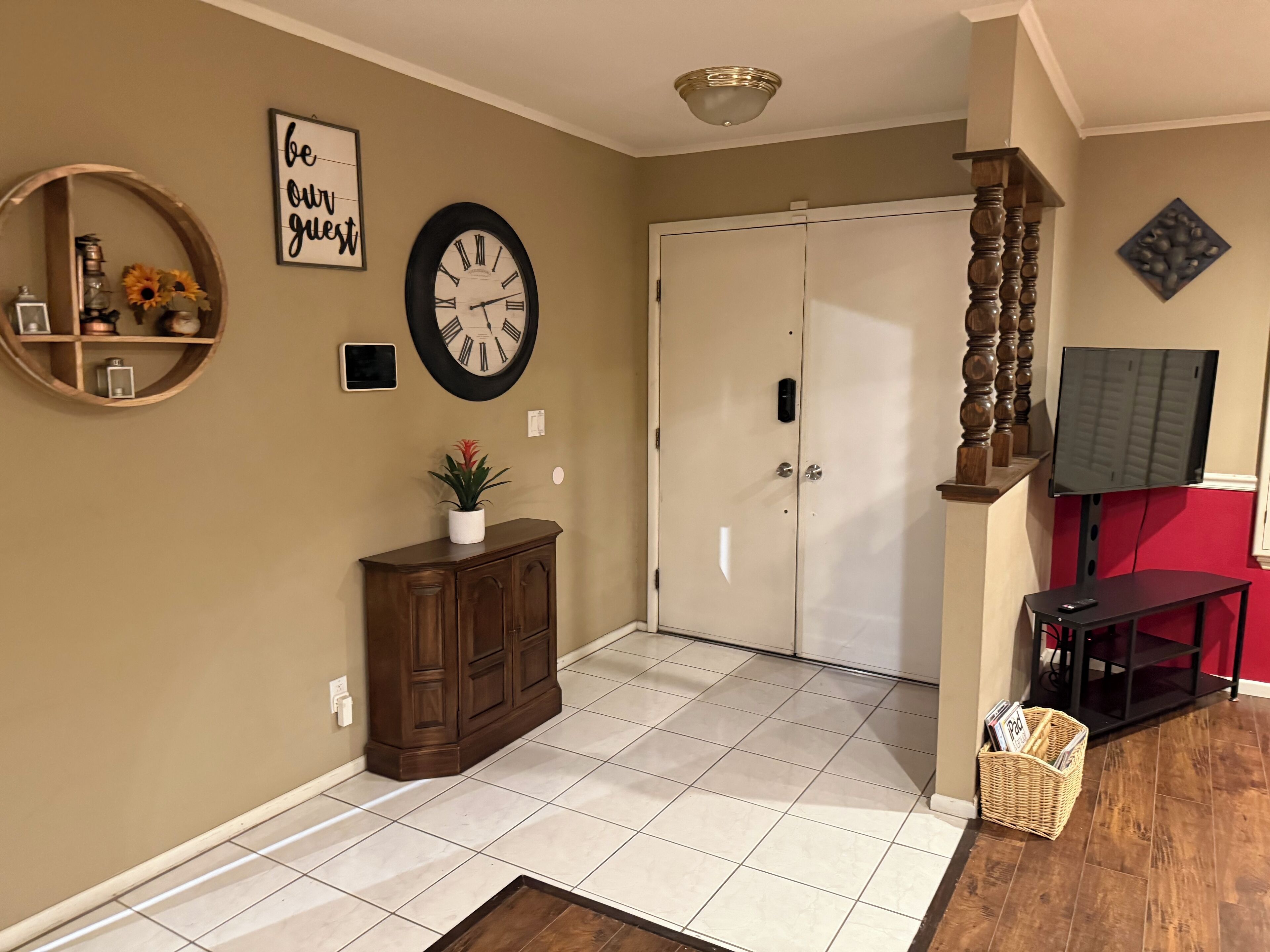 A well-lit hallway with a clock, a decorative sign, a cabinet, and a television.