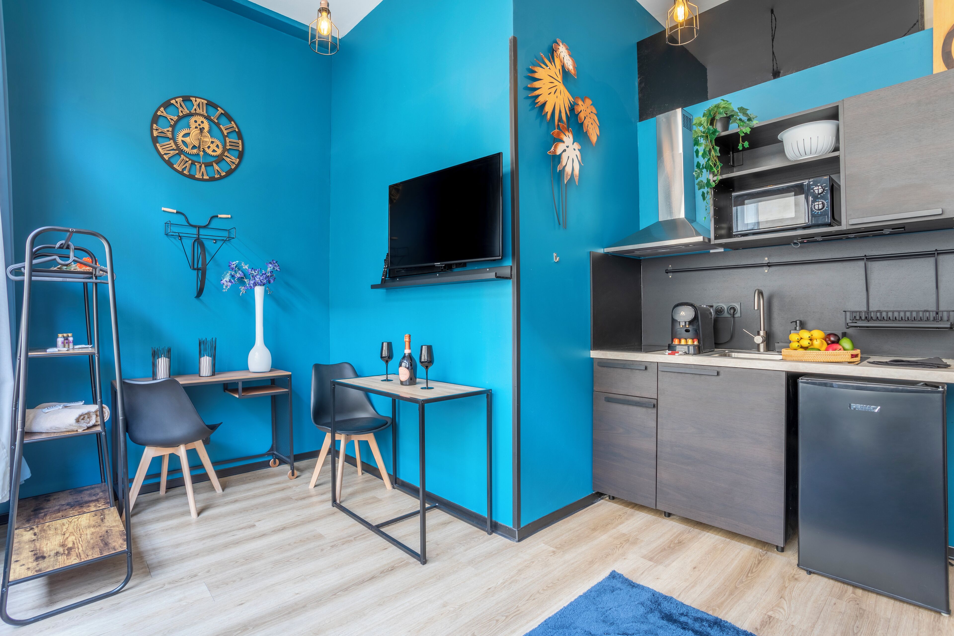 Una cocina compacta con pared azul, televisor montado, microondas y refrigerador.