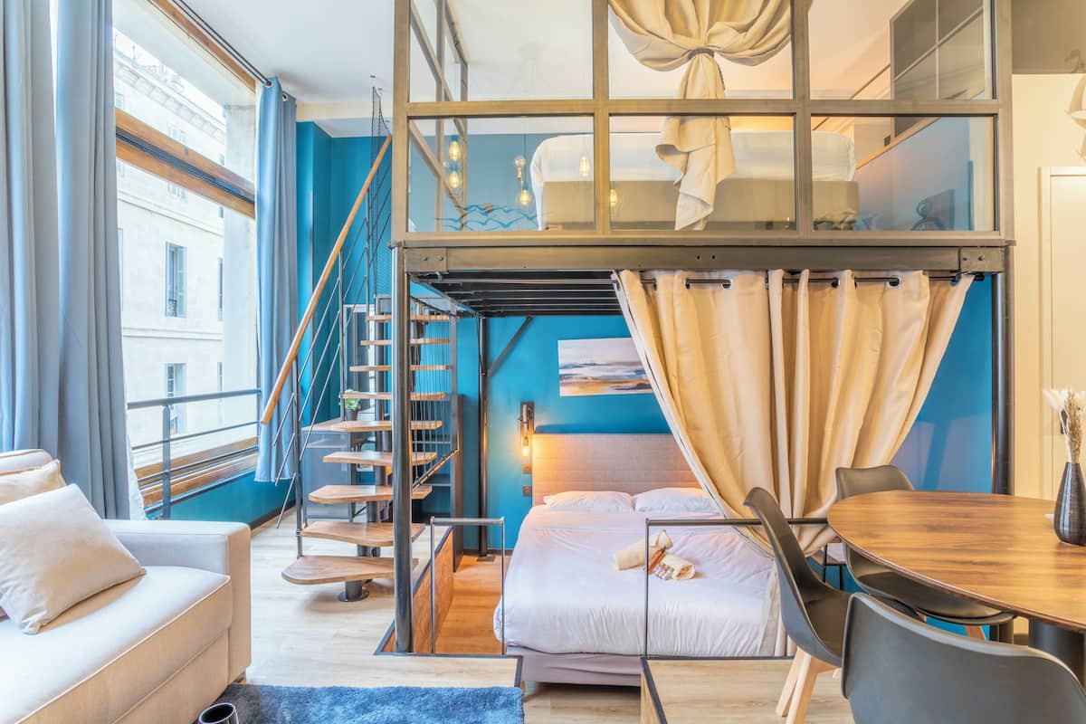Un dormitorio estilo loft moderno con una cama litera, un comedor y una escalera que lleva a un nivel superior.