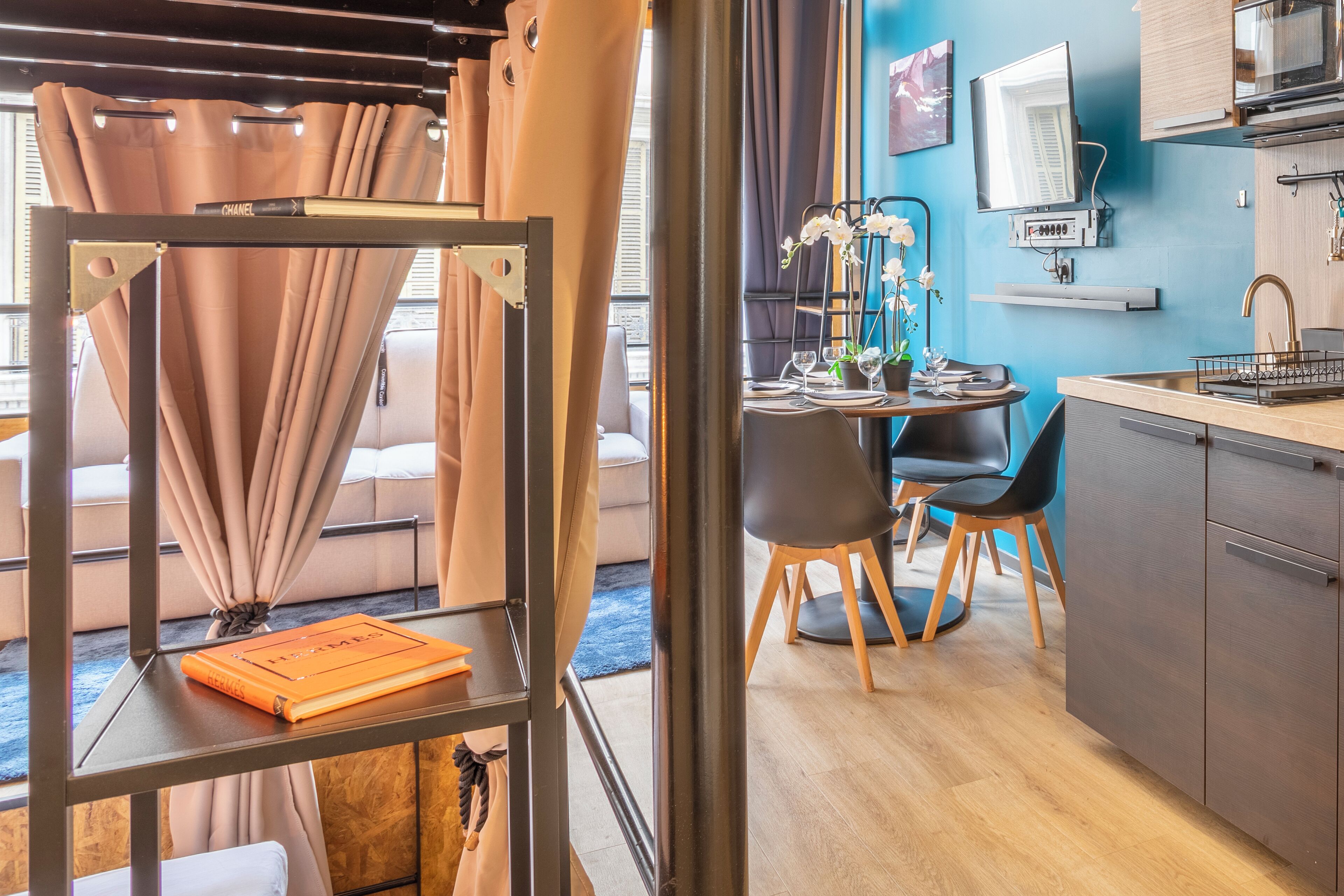 Een moderne keuken met een ingebouwde magnetron, een spoelbak en een aanrecht. Er is een zithoek met een tafel en stoelen, en een boekenkast met een boek.