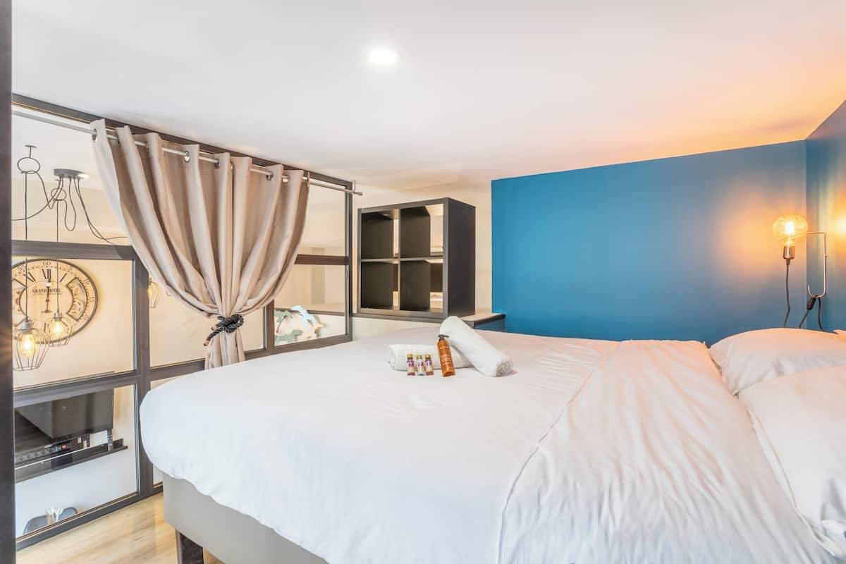 Una habitación de hotel moderna con una cama grande, una pared azul de acento, un reloj y una nevera pequeña.