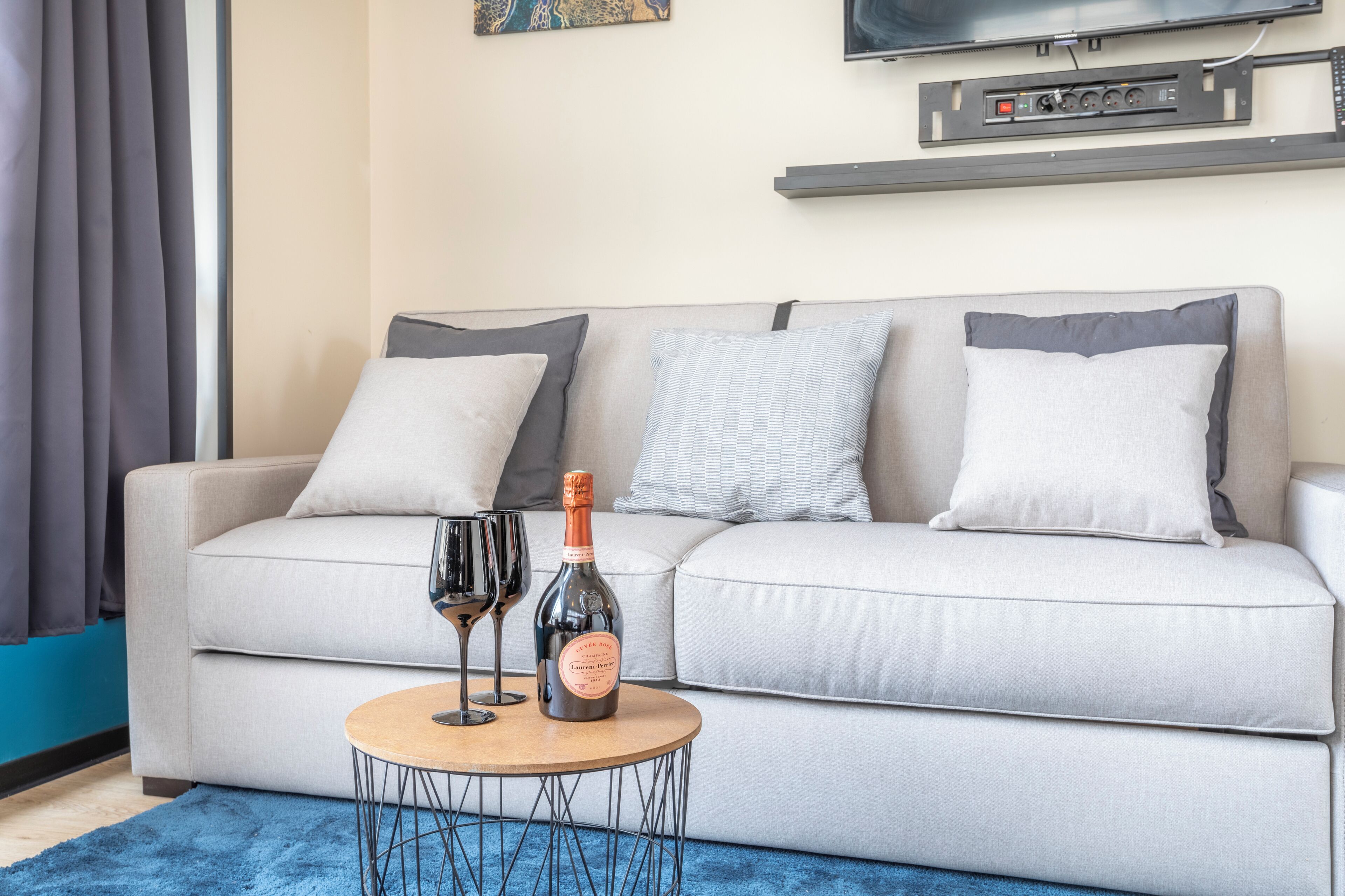 Ein modernes Wohnzimmer mit einer Couch, zwei Kissen, einer Champagnerflasche und zwei Weingläsern auf einem runden Couchtisch.