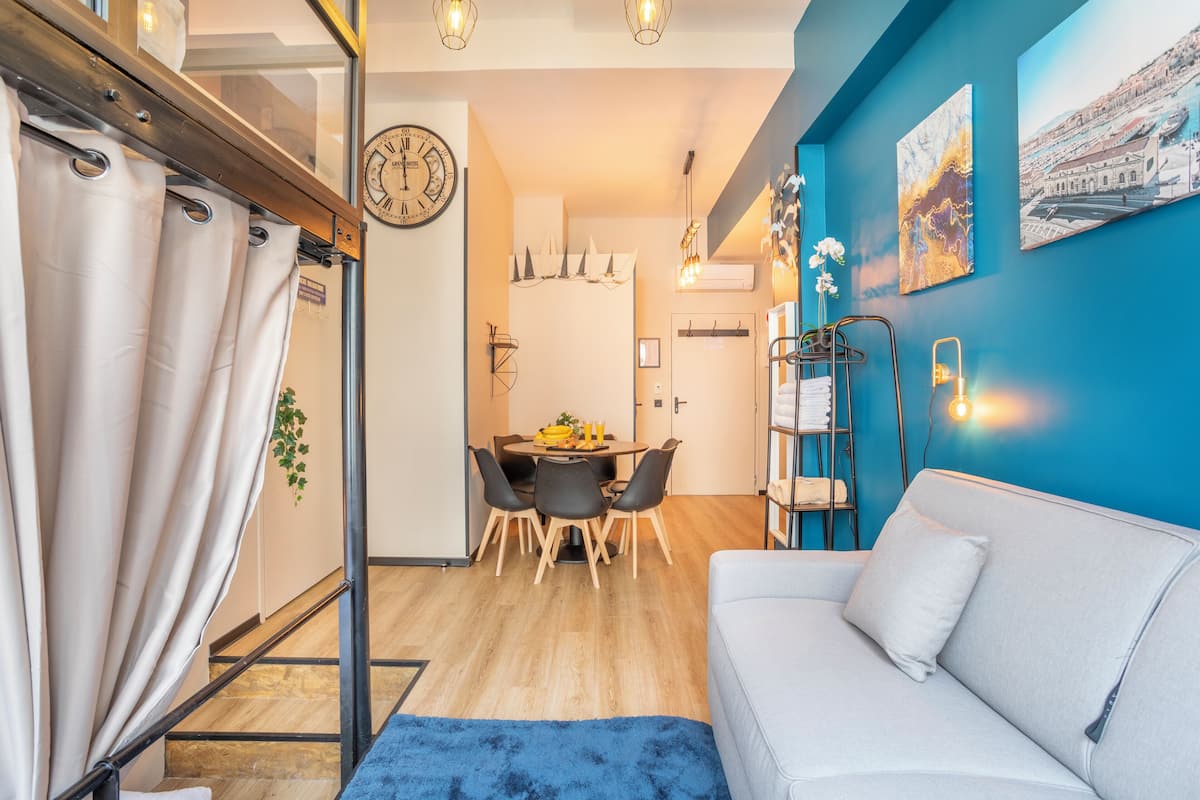 Una sala de estar moderna con una pared azul acento, un sofá blanco y un comedor con una mesa redonda y sillas.