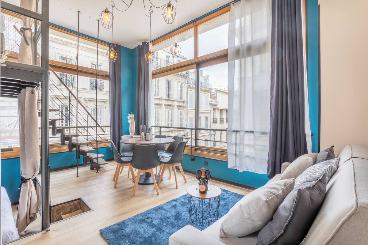 Una sala de estar moderna con un ventanal grande, un área de comedor y una escalera que lleva a un piso superior.