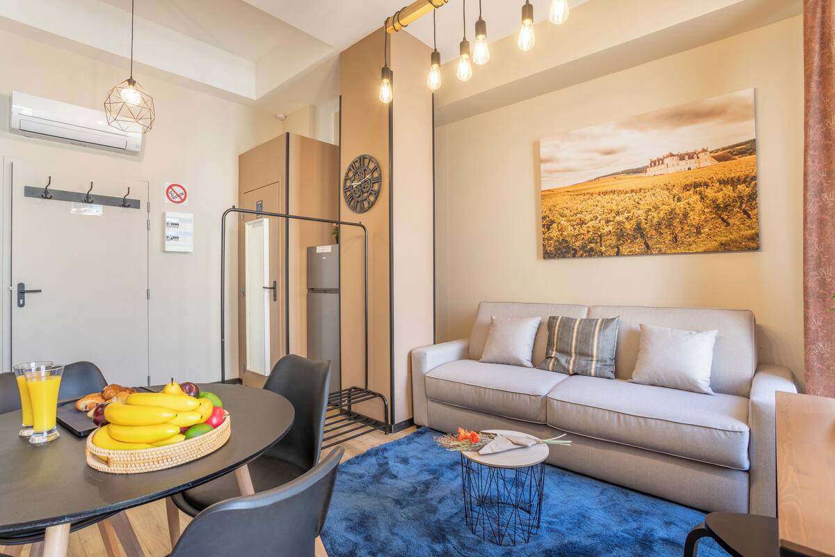 Una sala de estar moderna con un sofá, una mesa de comedor con fruta y un cuadro de un paisaje.