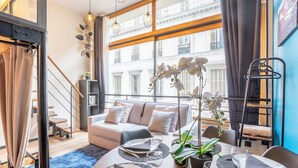 Una sala de estar moderna con un sofá, una mesa de comedor preparada para dos personas y una escalera que conduce a un piso superior.