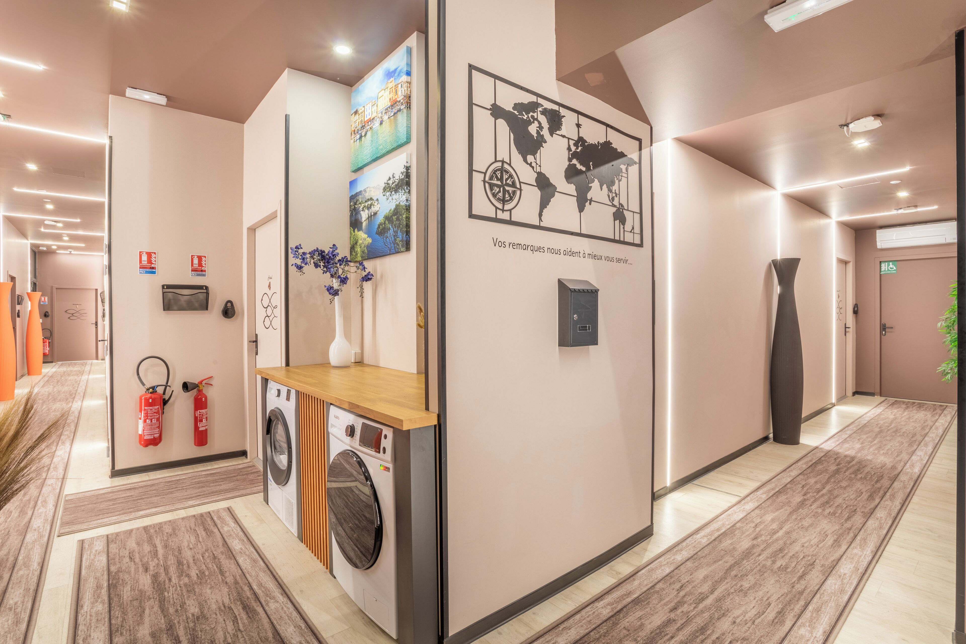 Un couloir d’hôtel avec un lave-linge, un extincteur et une carte du monde accrochée au mur.