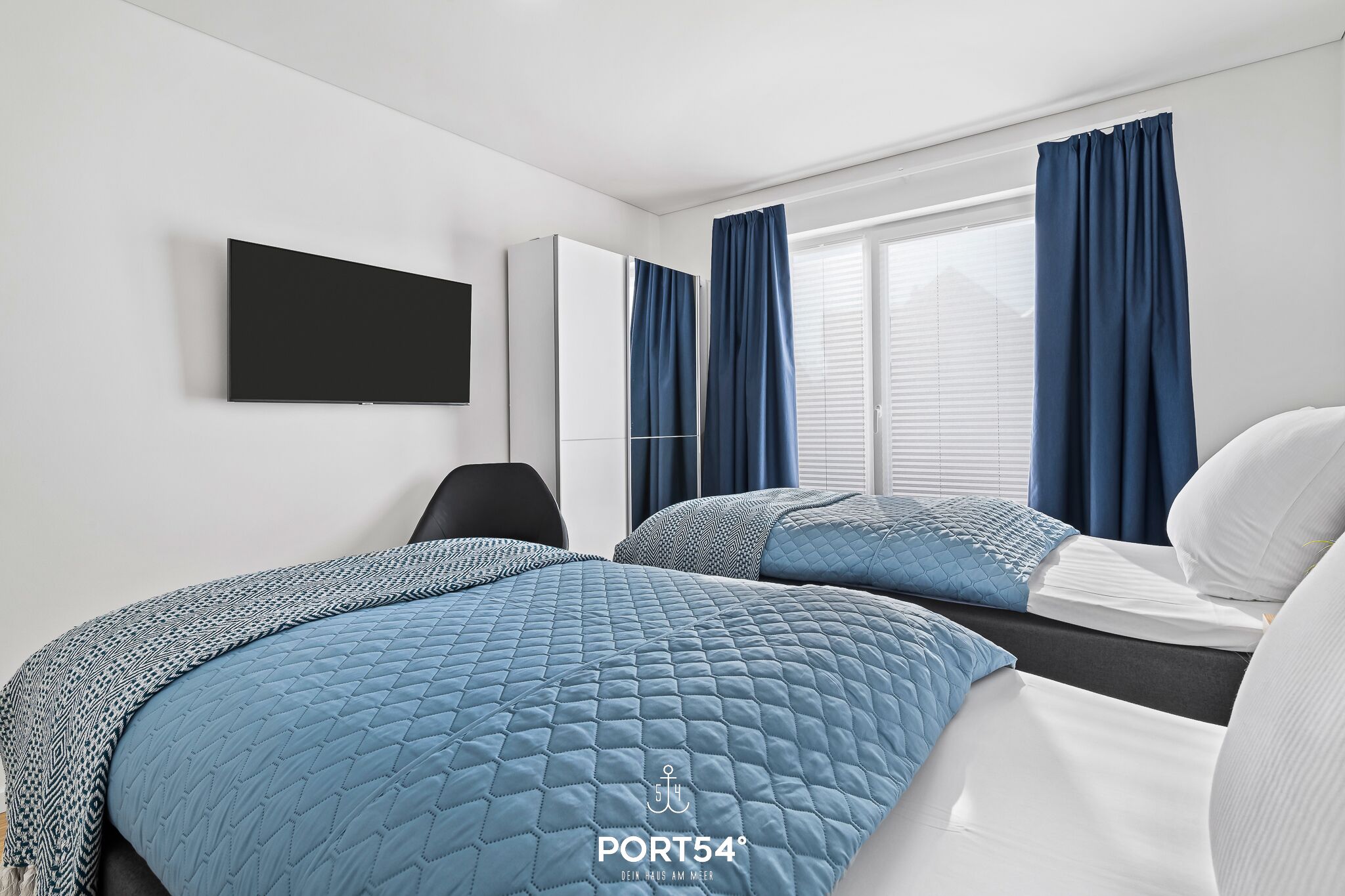A hotel room with two beds, a TV mounted on the wall, and a window with curtains.