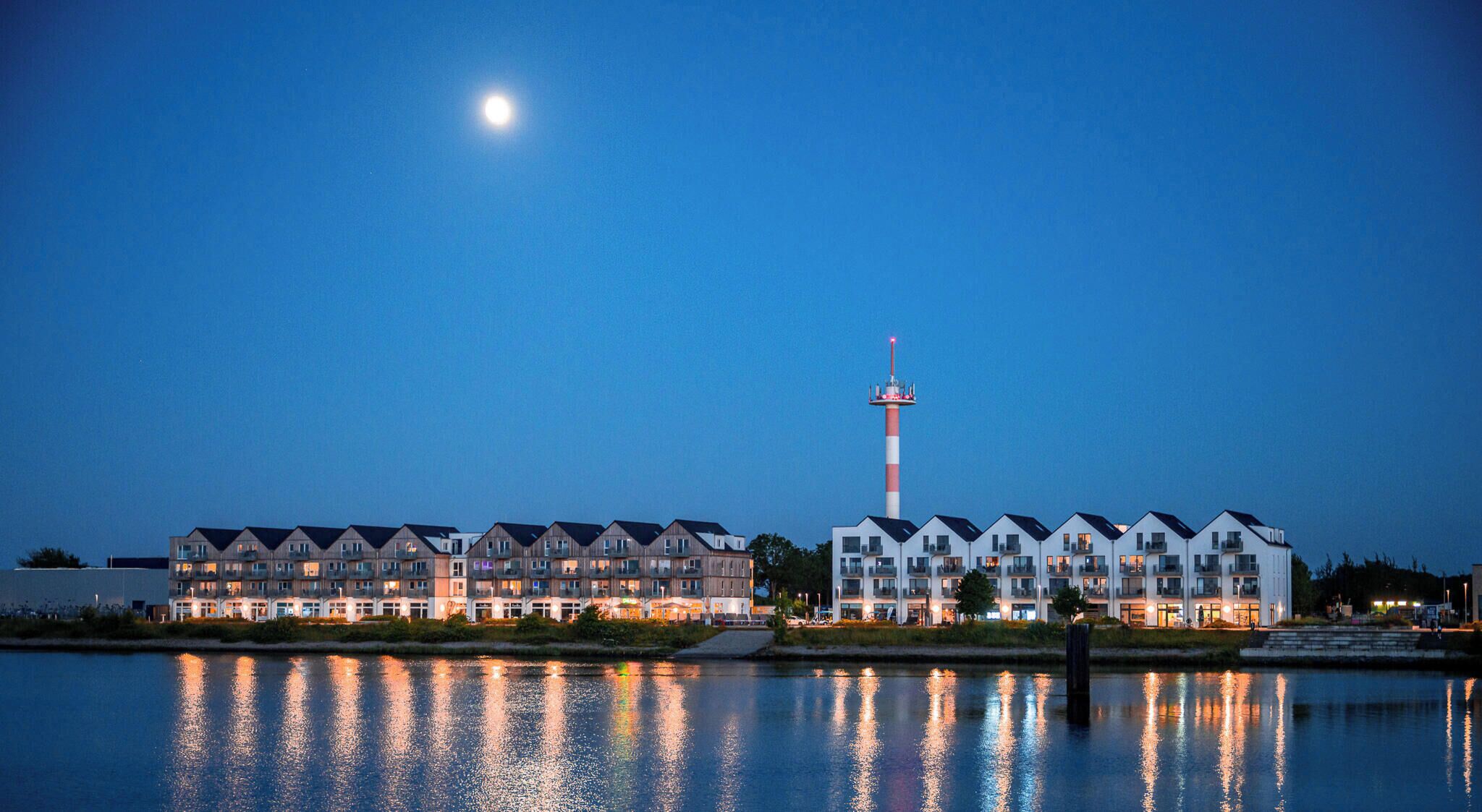 A waterfront hotel with multiple buildings, a prominent tower, and a calm reflective water surface.