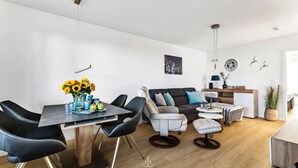 A modern living space with a dining area, a sofa, and a small kitchenette. - Leicht Matrose - Fireplace, Terrace, Infrared Sauna, Shower, Washing Machine (Olpenitz)