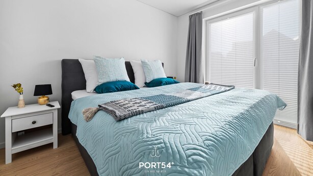 Un dormitorio moderno con cama, mesita de noche, lámpara y ventana con persianas.