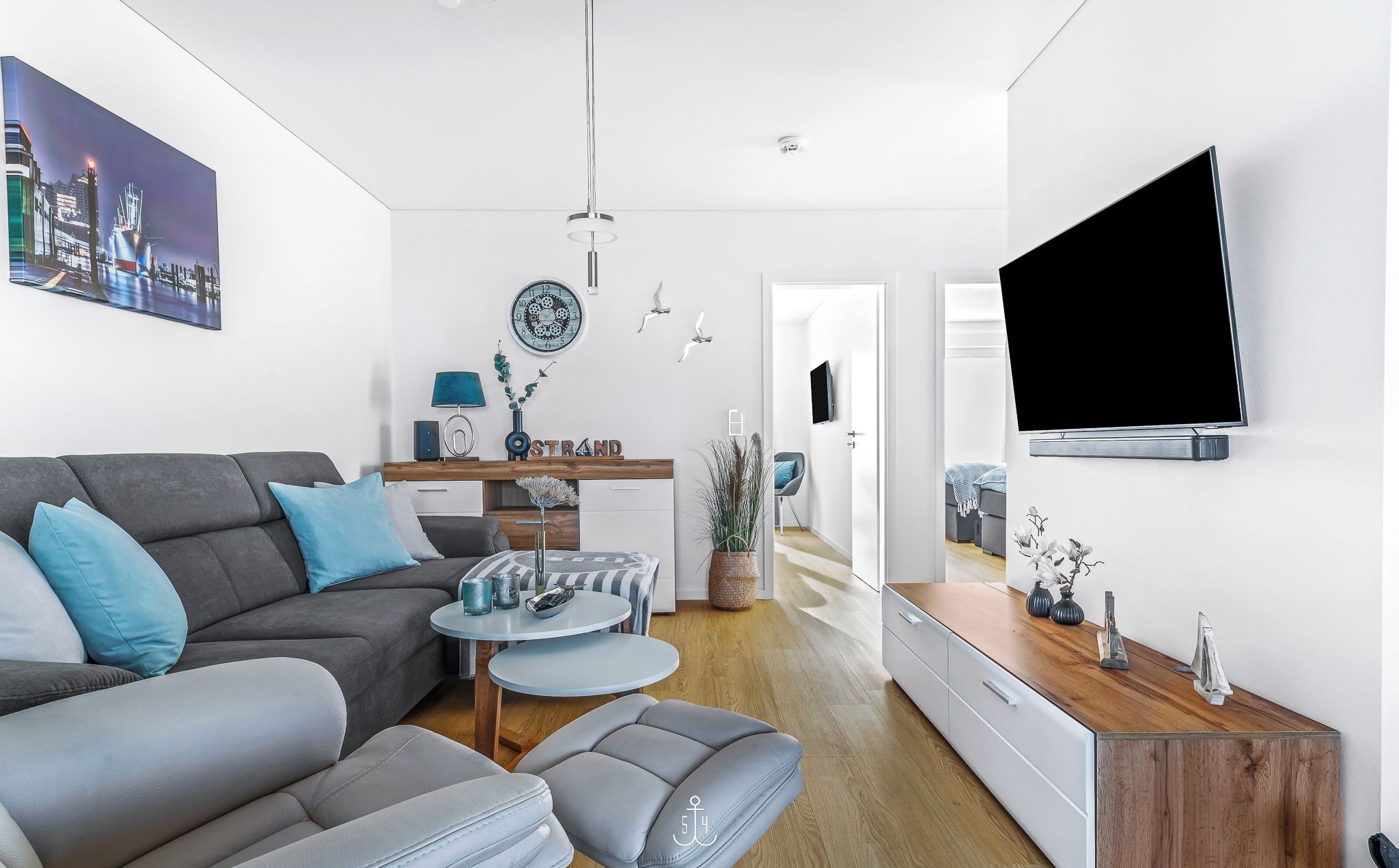 En moderne stue med en grå sofa, et sofabord og et fjernsyn monteret på væggen.