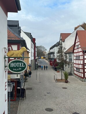 A cobblestone street with a hotel sign, traditional half-timbered buildings, and pedestrians. - Hotel Goldenes Lamm (Idstein)