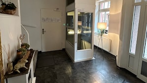 A modern living room with a sofa, a small table with decorative items, a glass door leading to a kitchen, and a view of the outside through a window. - Hotel Goldenes Lamm (Idstein)