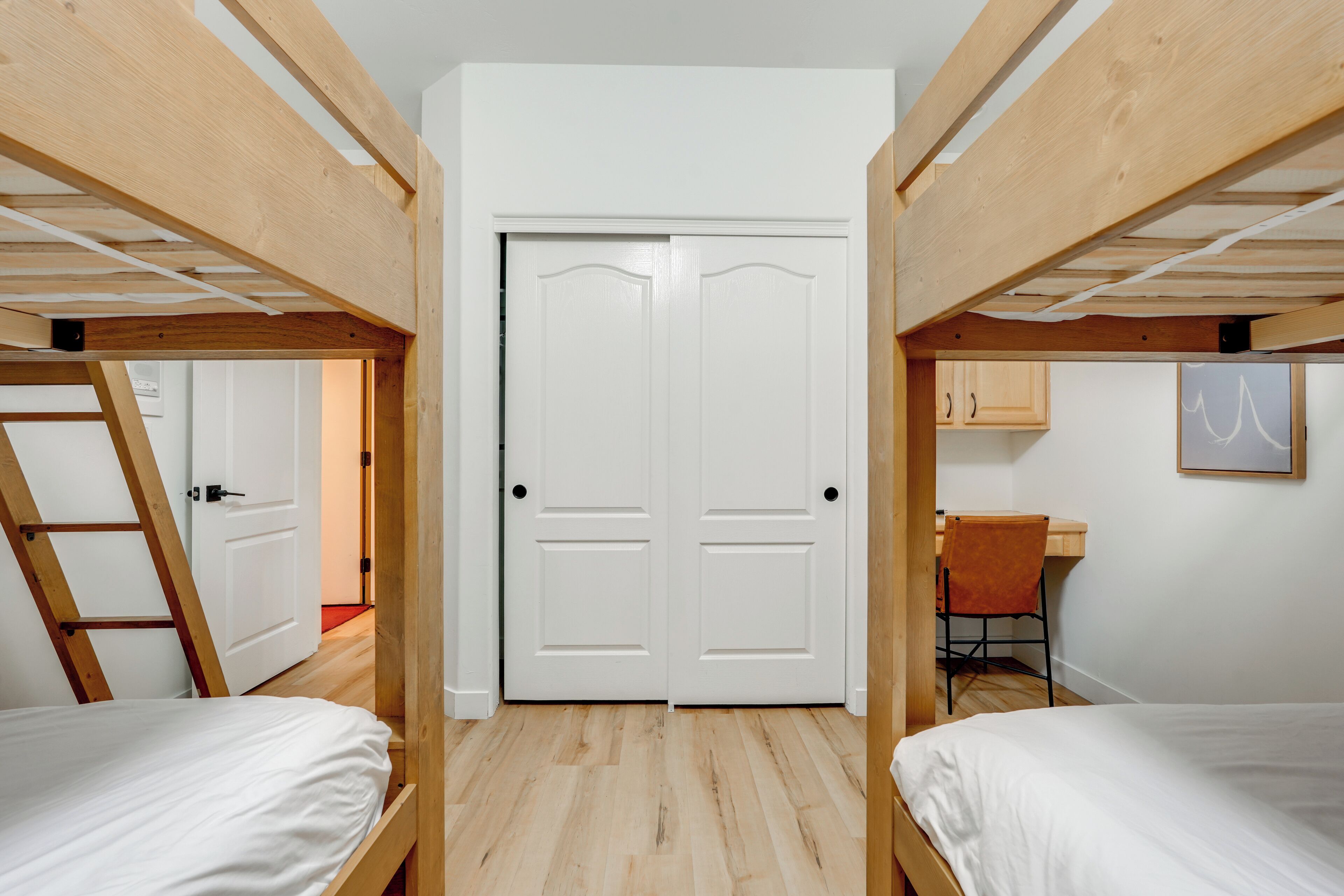 A room with two bunk beds, a white door, a desk with a chair, and a small cabinet.