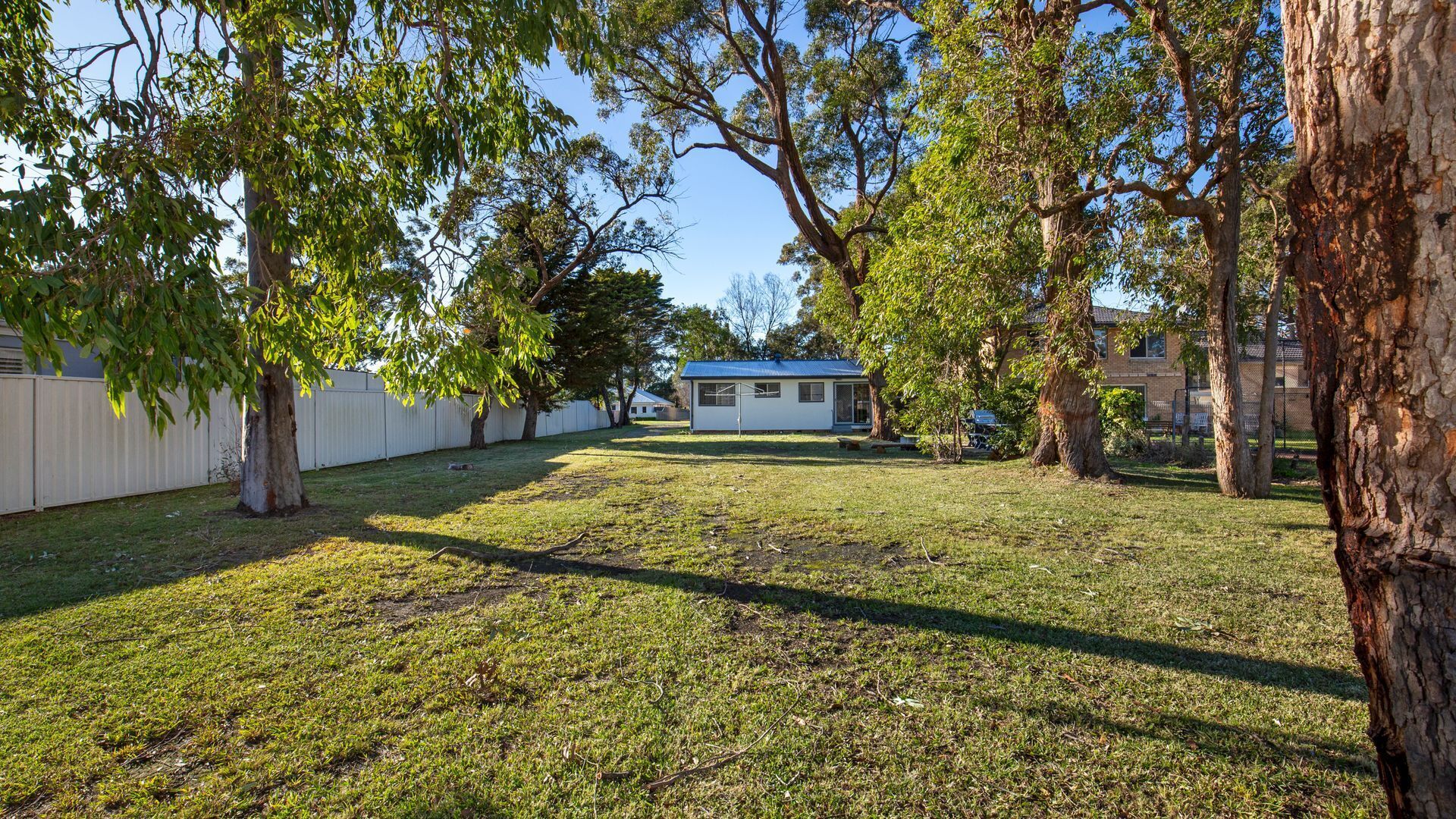 A backyard with a small house, surrounded by trees and a white fence.