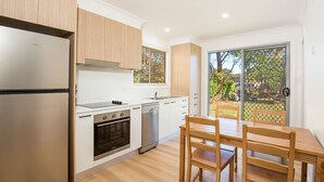 Une cuisine moderne avec des meubles blancs, des appareils en acier inoxydable et un coin repas comprenant une table et des chaises en bois.