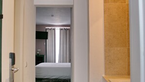 A hotel room with a bed, a bathroom with a bathtub, and a hallway leading to another room.