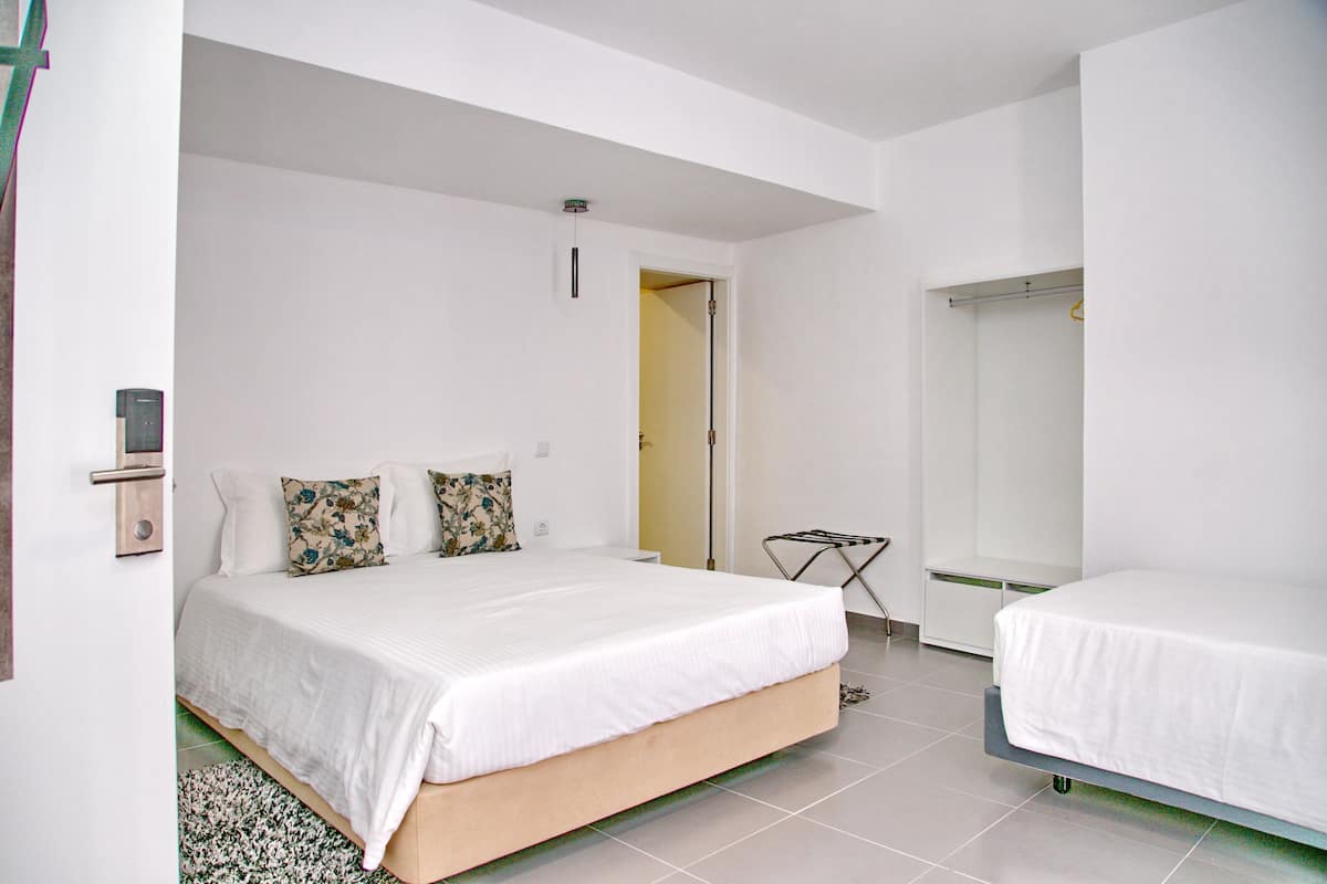A bedroom with a bed, a bedside table, a mirror, and a door leading to another room.