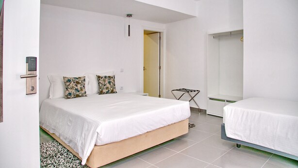 A bedroom with a bed, a bedside table, a mirror, and a door leading to another room.