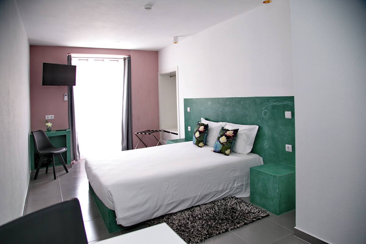 A bedroom with a bed, a desk, a chair, and a TV.