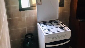 Una cocina compacta con estufa a gas, un refrigerador pequeño y una ventana sobre la estufa.