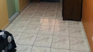 Una habitación con suelo de baldosas, puerta de madera, una pequeña mesa de madera y una cortina.