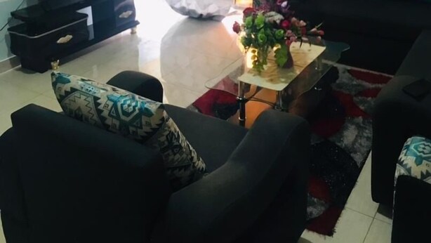 Una sala de estar con un sofá, una mesa de centro con un florero, un televisor sobre un mueble bajo y una ventana con cortinas.