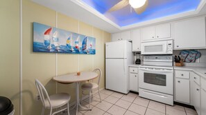 A compact kitchen with white cabinets, a microwave, an oven, and a refrigerator. There is a small dining table with two chairs. - Endless Summer Getaway at Sandarac (Fort Myers Beach)