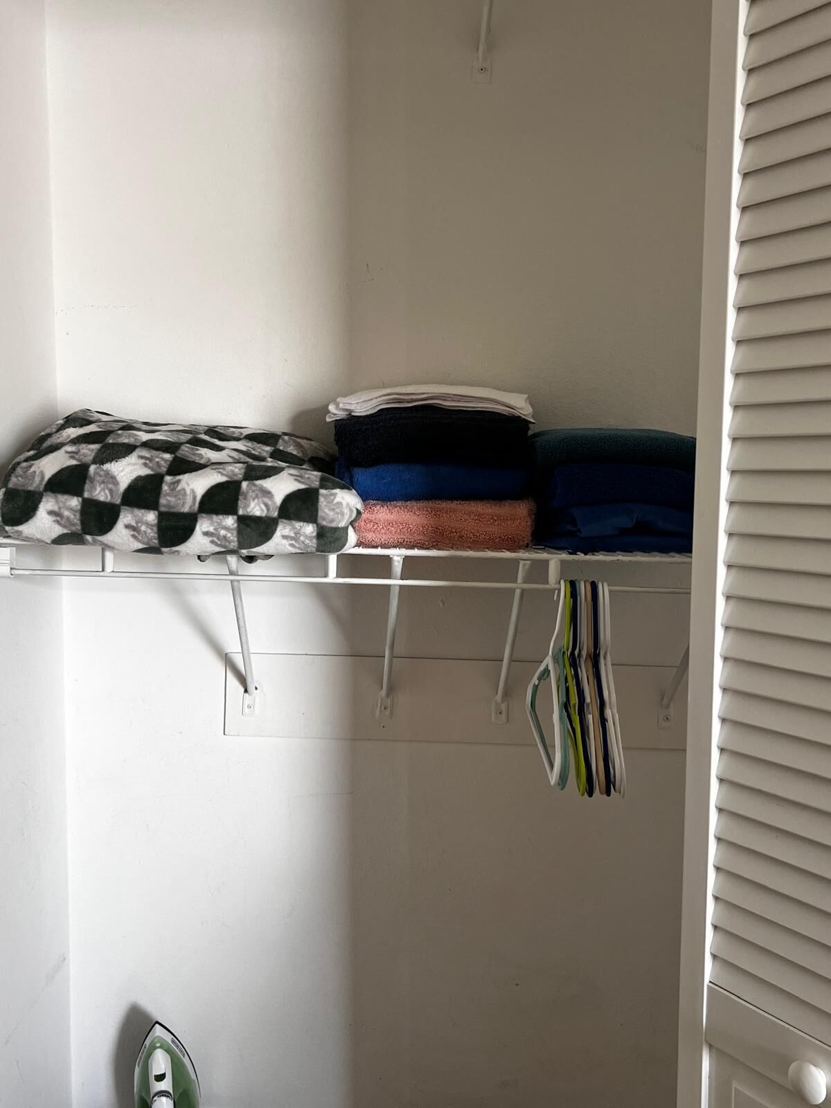 Een kast met opgevouwen kleding op een plank en hangende items eronder.