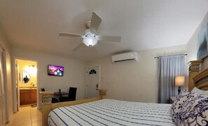 A hotel room with a bed, a ceiling fan, an air conditioning unit, a television, a door, and a bathroom visible through an open door.