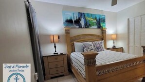 A bedroom with a wooden bed, two bedside tables with lamps, a painting above the bed, and a set of white closets. - #9 Hideaway (Tampa)