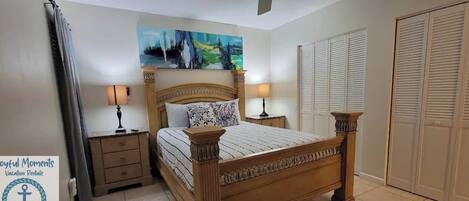 A bedroom with a wooden bed, two bedside tables with lamps, a painting above the bed, and a set of white closets.