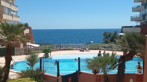 Ein Poolbereich mit Blick auf das Meer, umgeben von Palmen und einem Gebäude.