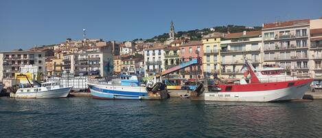 A harbor with boats docked, a prominent church tower, and colorful buildings in the background.