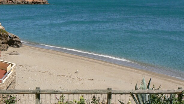 Ein Strand mit einer Holzlattenveranda, sandigem Ufer und einem Felsvorsprung im Hintergrund.