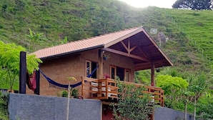 A rustic wooden house with a red roof, surrounded by lush green grass and a hill in the background. - Chalet in the Serra da Mantiqueira mountains in São Bento do Sapucai, near southern Minas Gerais.  (São Bento do Sapucaí)