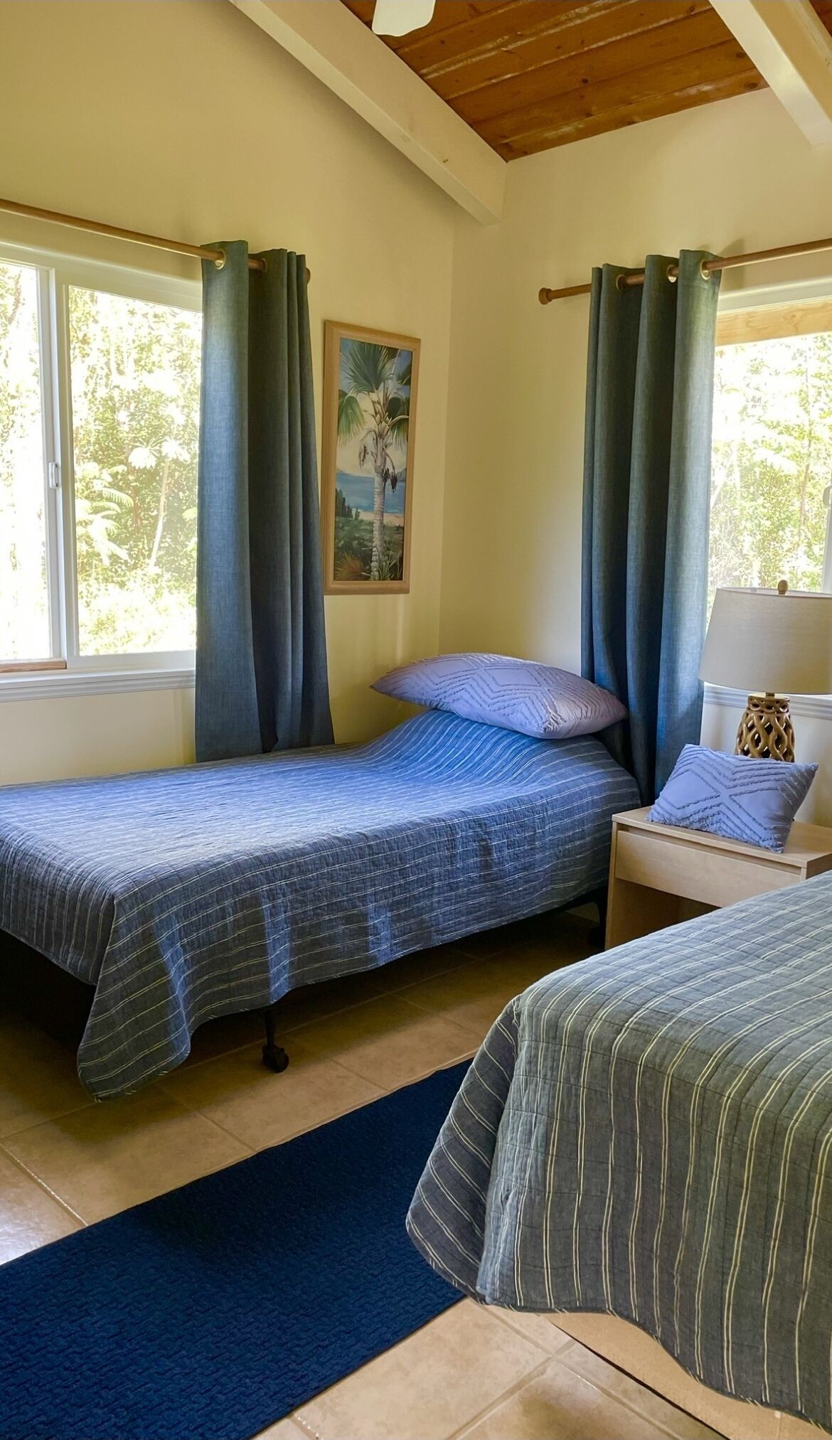 Quarto com duas camas, uma mesinha de cabeceira, um abajur e um quadro na parede.
