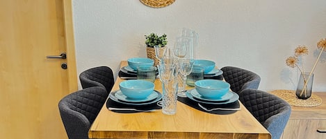 A dining table set with blue bowls and glasses, surrounded by dark upholstered chairs.