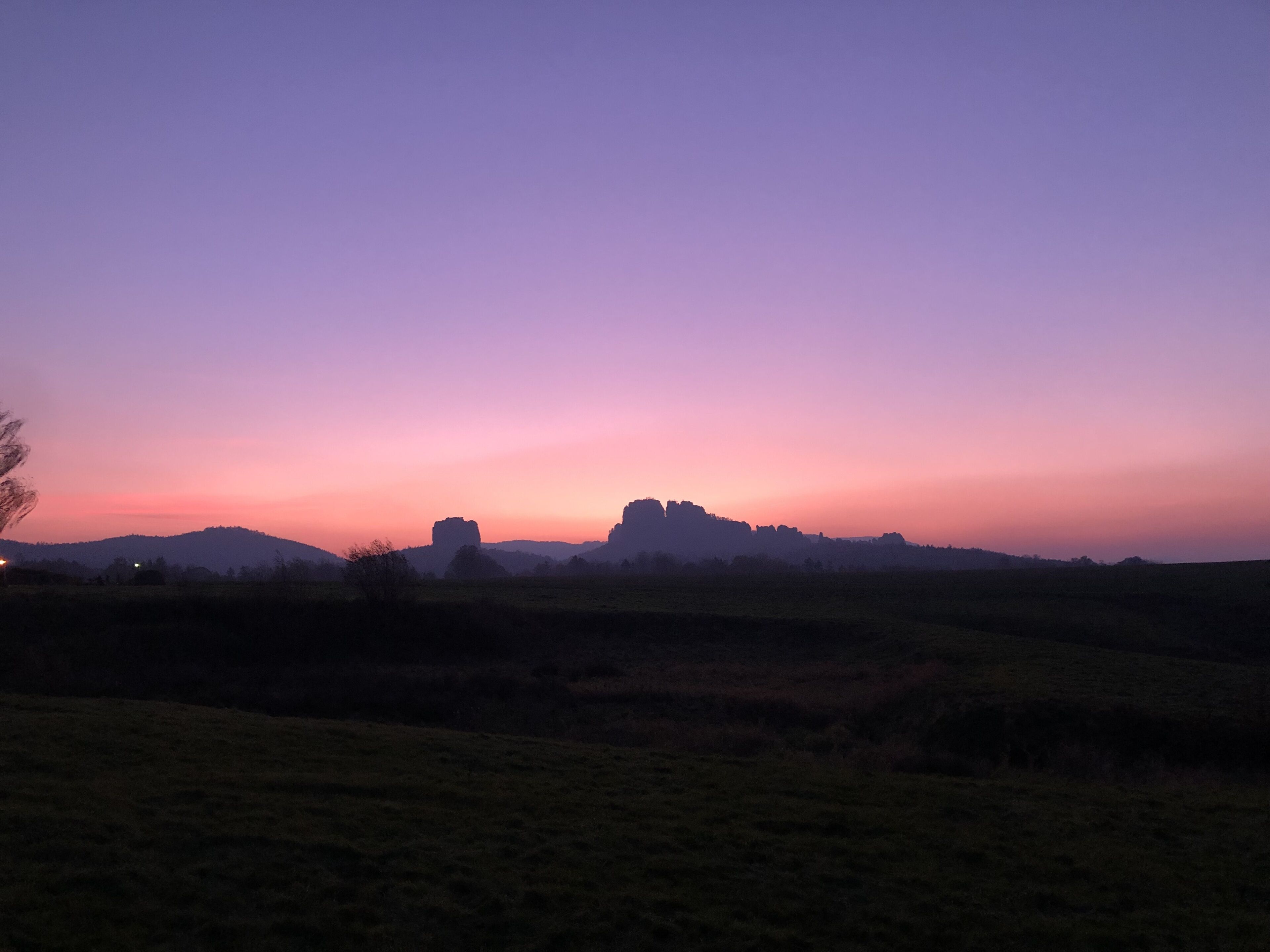 A sunset over a hilly landscape with a silhouette of a castle-like structure.