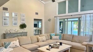 A spacious living room with a large sectional sofa, a coffee table, and a ceiling fan. There are framed pictures on the wall and a plant on a console table. - ~ Private Beach Access! ~ East A1A ~~ Sun, Sea, Pool, Relax!  (Vero Beach)