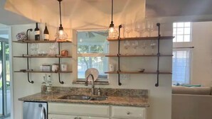 A kitchen with white cabinets, a stainless steel refrigerator, and a granite countertop. There are hanging shelves above the sink and a window with a view of the outdoors. - ~ Private Beach Access! ~ East A1A ~~ Sun, Sea, Pool, Relax!  (Vero Beach)