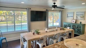 A dining area with a wooden table, white chairs, a ceiling fan, and a view of a swimming pool through large windows. - ~ Private Beach Access! ~ East A1A ~~ Sun, Sea, Pool, Relax!  (Vero Beach)
