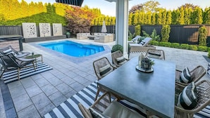Eine überdachte Terrasse mit Pool, Gartenmöbeln und Blick auf einen angelegten Garten.
