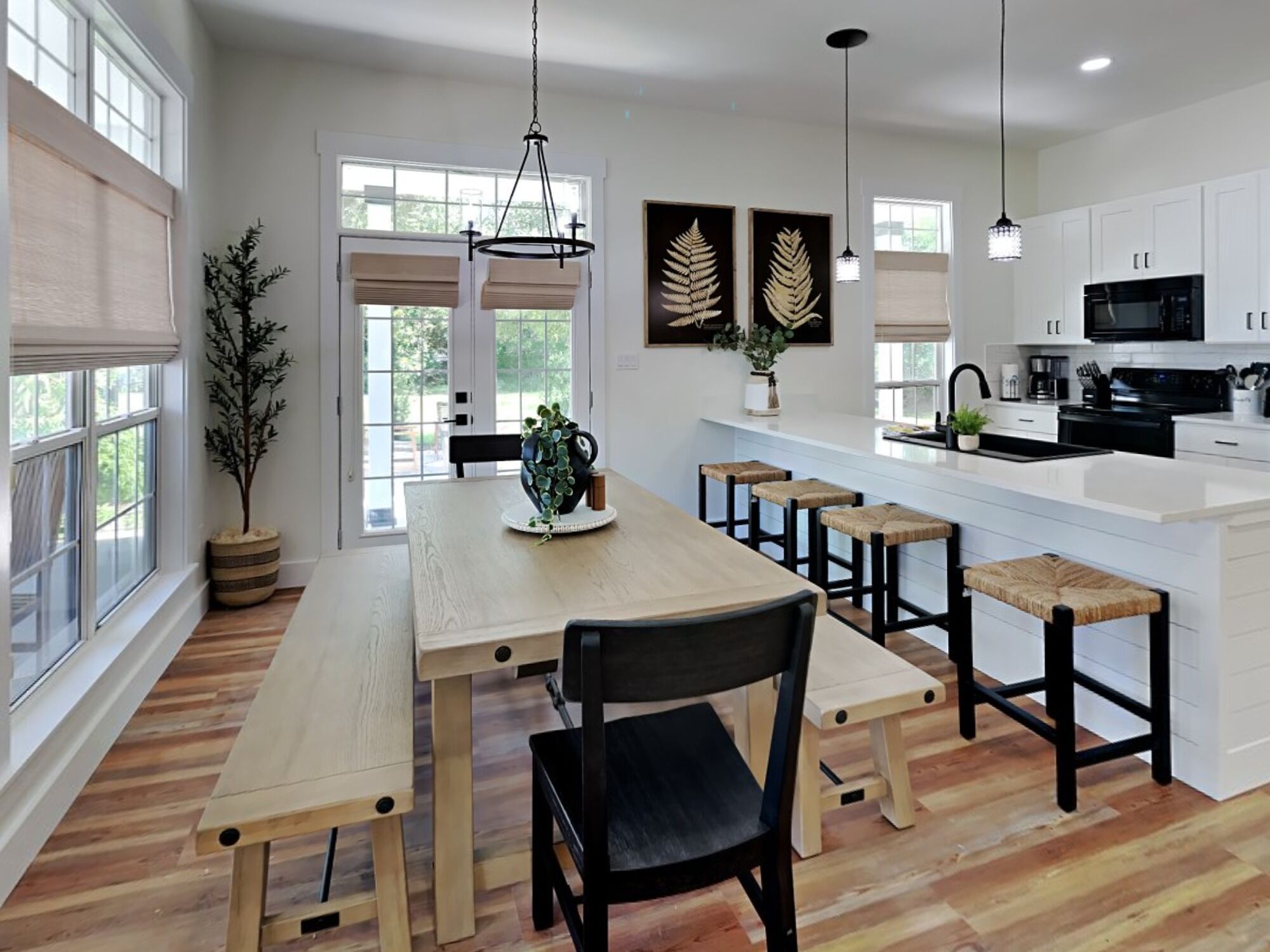 A modern kitchen with white cabinets, a wooden dining table with benches, and pendant lighting.