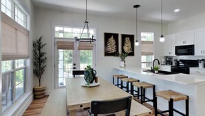 A modern kitchen with white cabinets, a wooden dining table with benches, and pendant lighting.