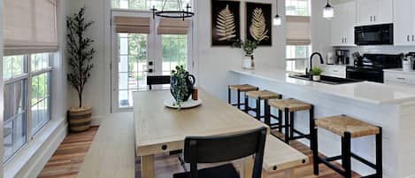 A modern kitchen with white cabinets, a wooden dining table with benches, and pendant lighting.